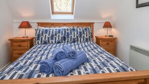 Un dormitorio con una cama de madera, dos mesitas de noche, una ventana y un radiador.