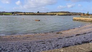 A beach with a rocky shoreline and calm water. - Crud yr Awel (Y Felinheli)