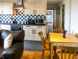 A compact kitchen with a microwave, stove, and checkered backsplash. There is a dining area with a table and chairs, and a sofa with a cushion.