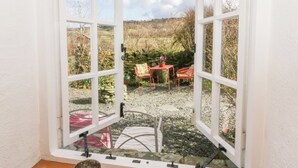 Une fenêtre ouverte donnant sur un jardin, où l’on aperçoit une table et des chaises.