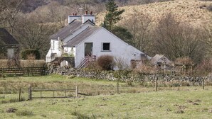 Une maison blanche avec un mur de pierre à l’avant, entourée d’un paysage rural.