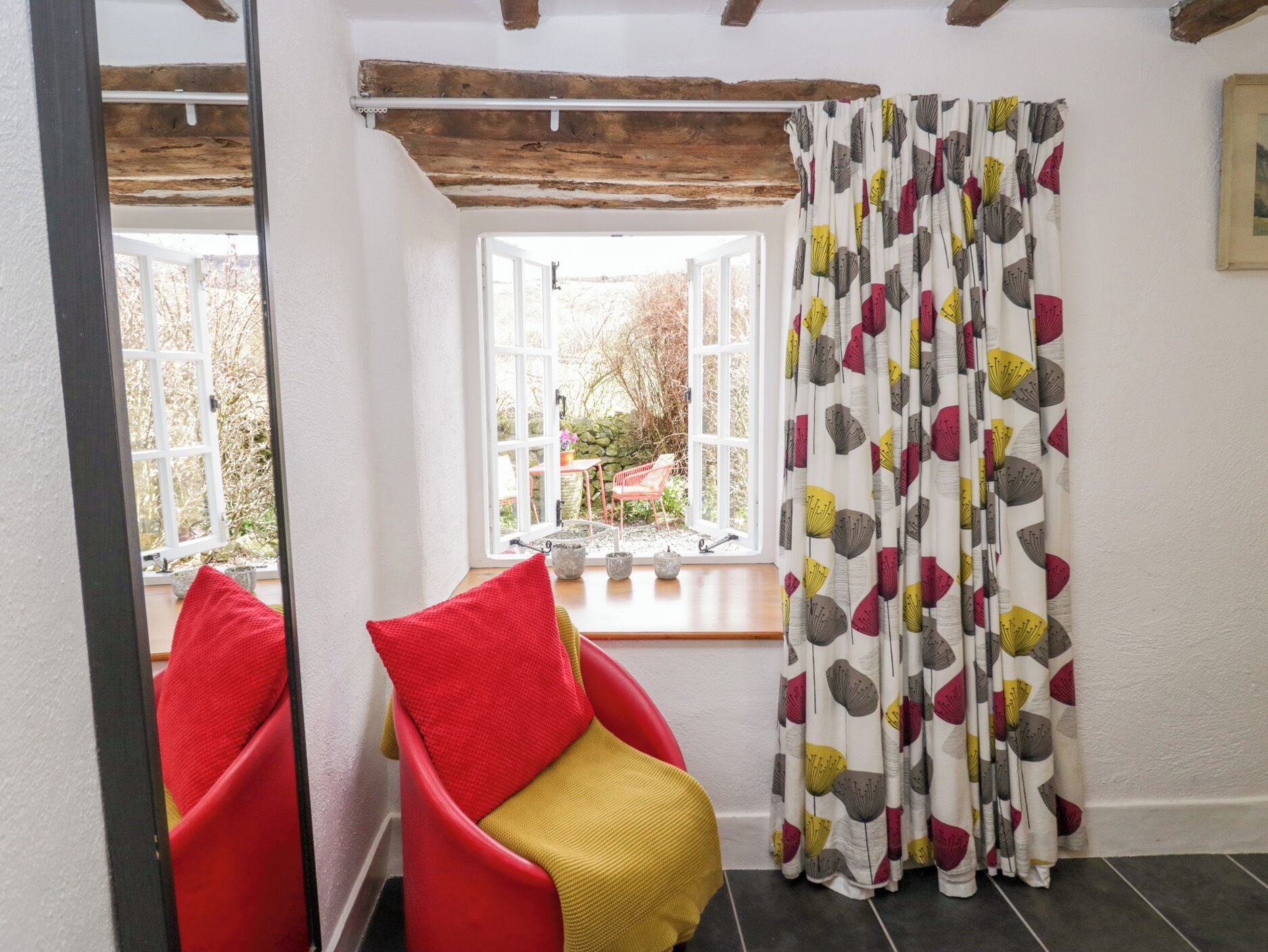 A room with a red chair, a yellow cushion, and a window with white curtains.