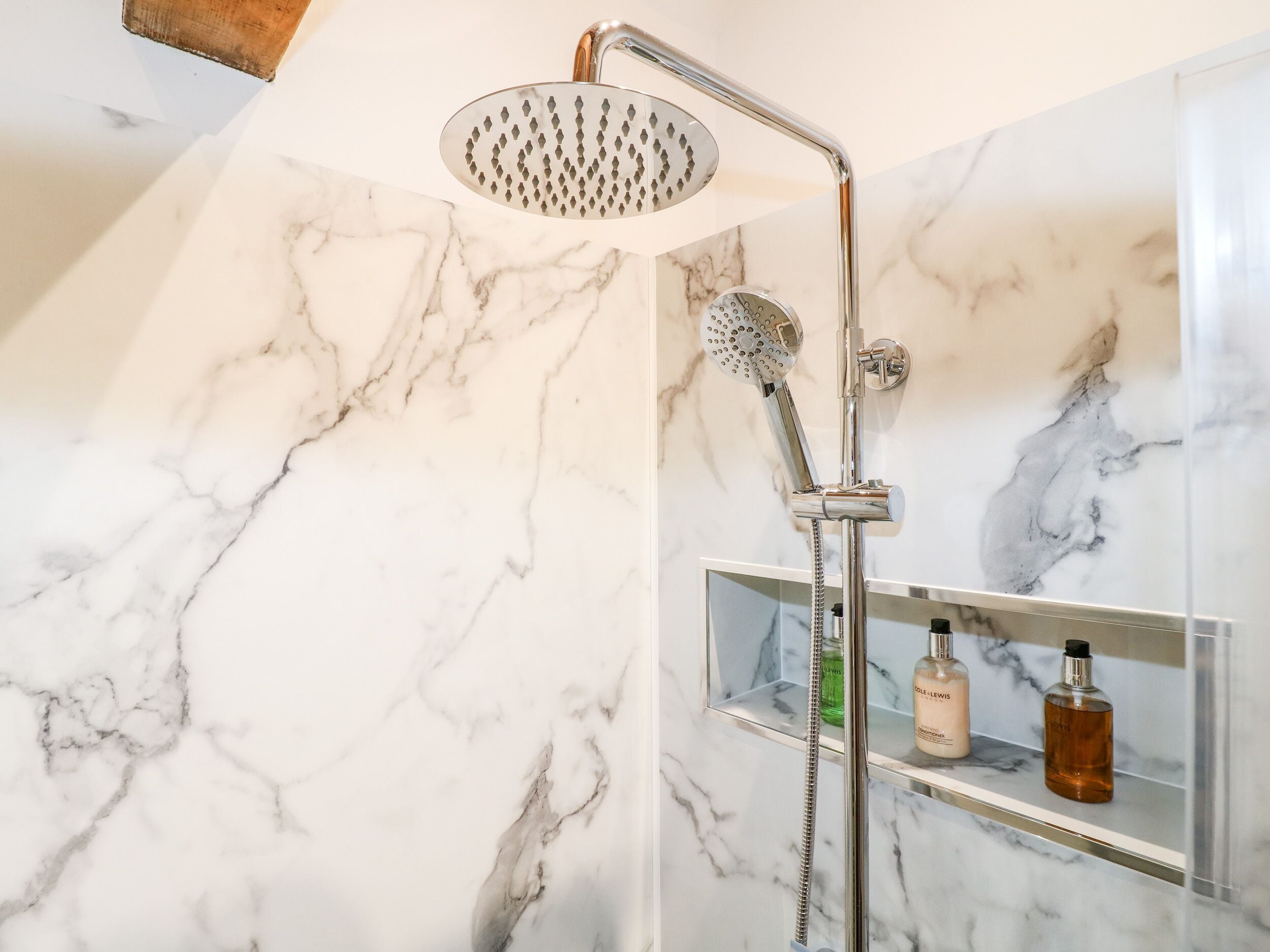 A modern bathroom with a shower, marble walls, and a shelf with toiletries.