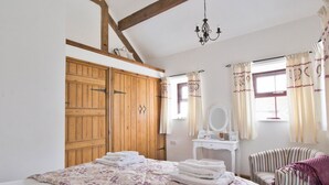 A bedroom with a bed, a vanity with a mirror, a chair, and wooden wardrobes.