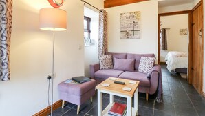 A living room with a sofa, ottoman, and a small table with a lamp and remote control.