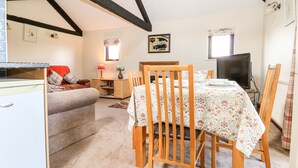 A cozy dining area with a wooden table set for four, a television, and a small cabinet with a lamp. - The Granary (Henfield)
