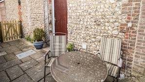 A stone wall with a wooden door, a potted plant, and two striped chairs around a round table. - The Granary (Henfield)