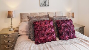 Ein Schlafzimmer mit einem Bett, zwei Nachttischen, einer Lampe auf jedem Tisch und einem gerahmten Kunstwerk an der Wand.