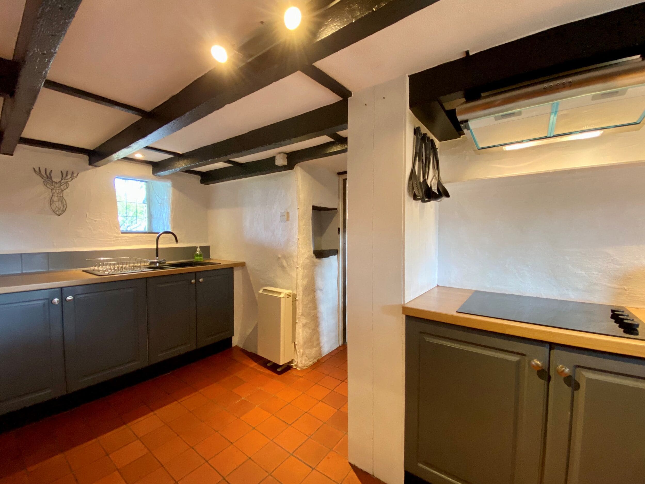 A kitchen with dark wooden beams, a window, a sink, and a refrigerator.