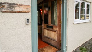 Eine Holztür mit einem Schild darüber, ein Fenster mit weißem Rahmen und ein kleiner Podeststufenaufgang zum Eingang.