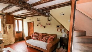 Ein gemütliches Zimmer mit einem braunen Sofa, Holzbalken, einer Steinwand und einer Treppe.