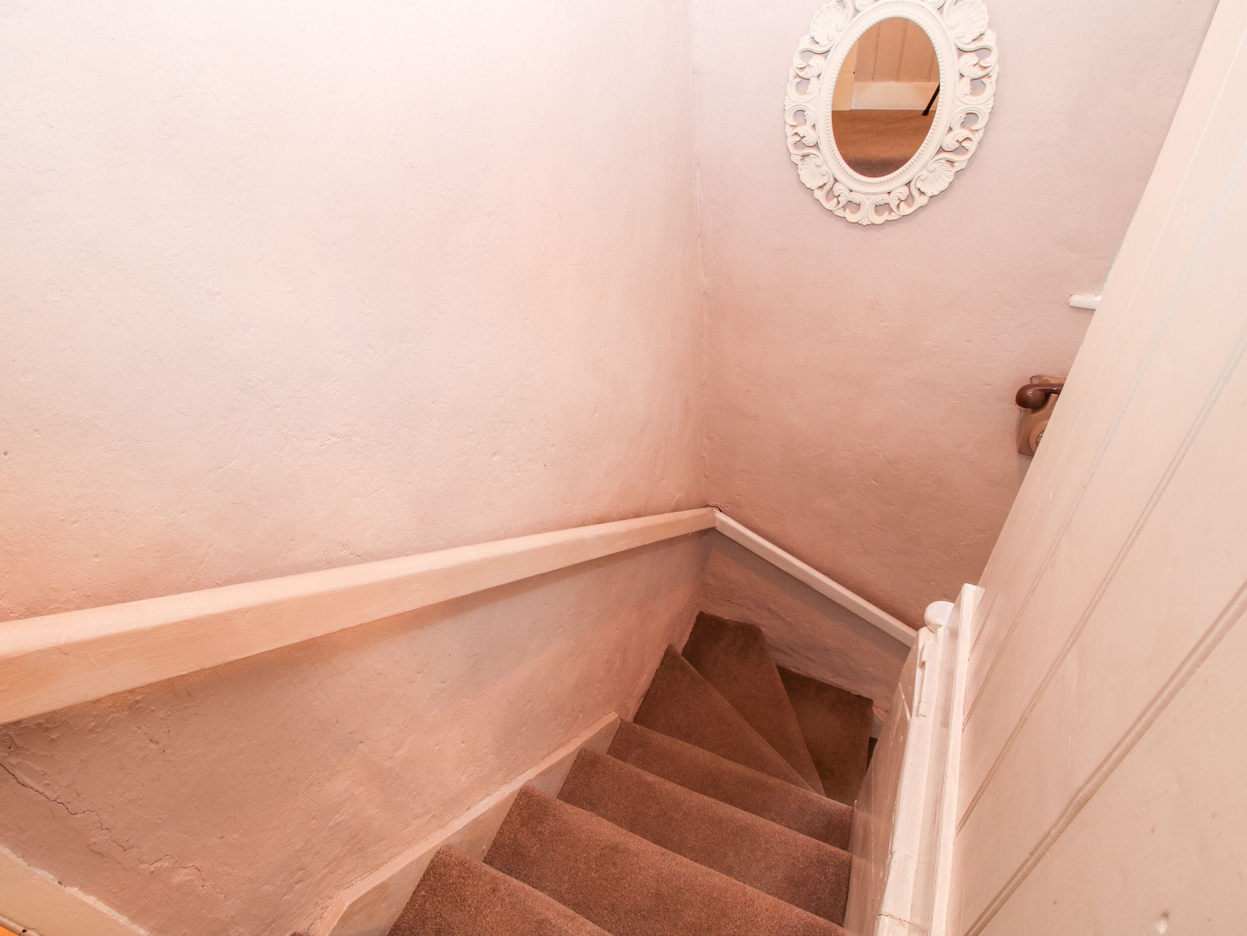Eine Treppe mit Geländer, einer weißen Wand und einem Spiegel.