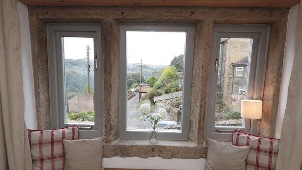 Une pièce chaleureuse avec une banquette intégrée située sous trois fenêtres, offrant une vue sur un charmant village.