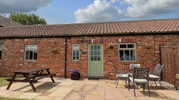 A brick building with a tiled roof, a green door, and a patio area with a picnic table and chairs.