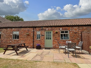 A brick building with a tiled roof, a green door, and a patio area with a picnic table and chairs. - Beacon (Saltburn-by-the-Sea)