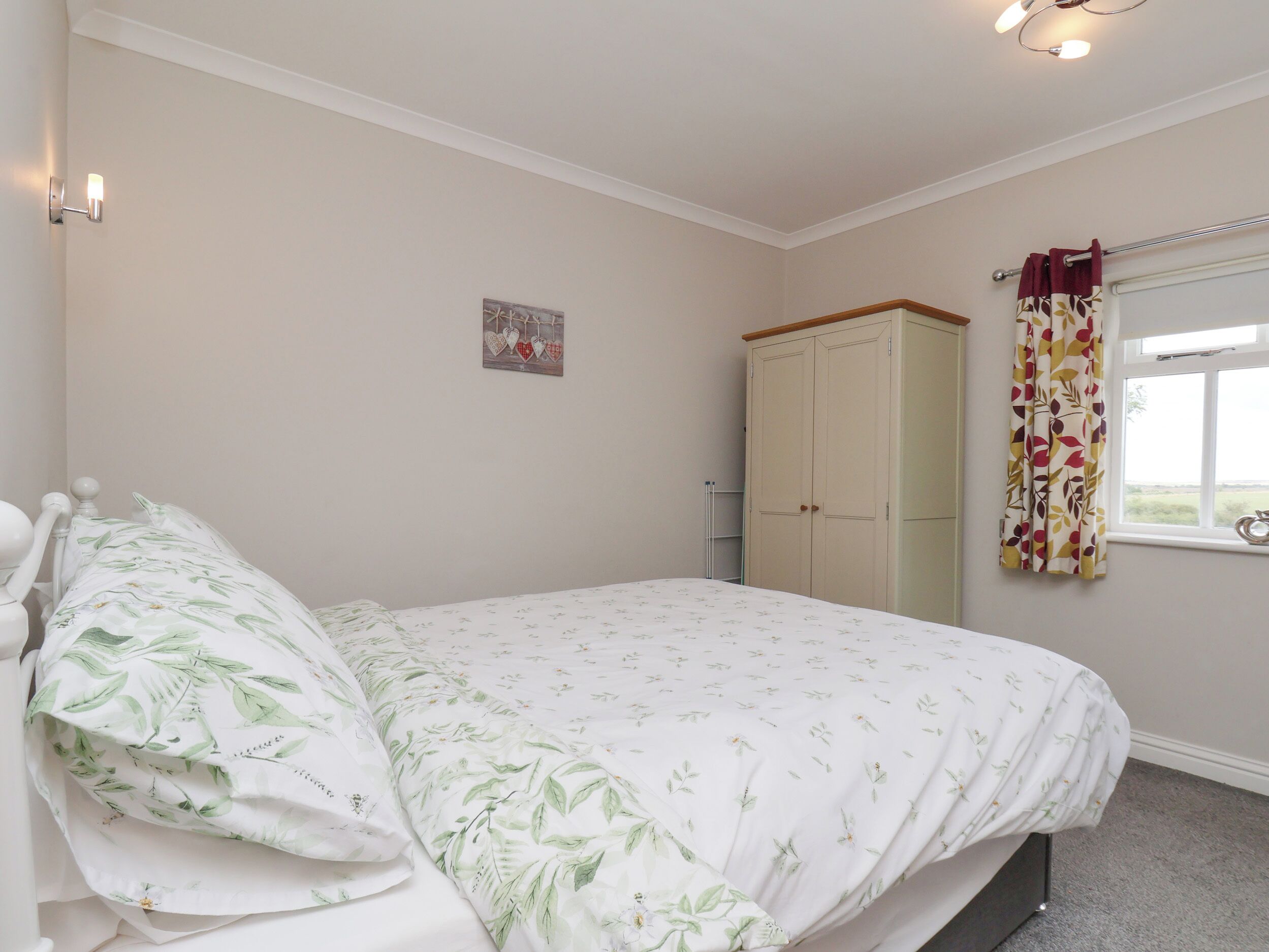 Un dormitorio con cama, armario, ventana con cortinas y lámpara fijada a la pared.