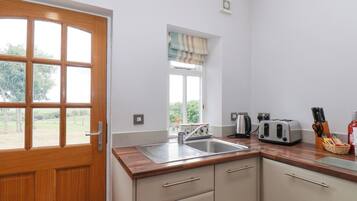 A kitchen with a wooden door, a window with curtains, a sink, a kettle, a toaster, and a knife block.