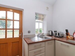 Une cuisine avec une porte en bois, une fenêtre avec des rideaux, un évier, une bouilloire, un grille-pain et un bloc à couteaux.