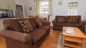 A living room with two brown sofas, a wooden coffee table, and a kitchen area with a microwave.