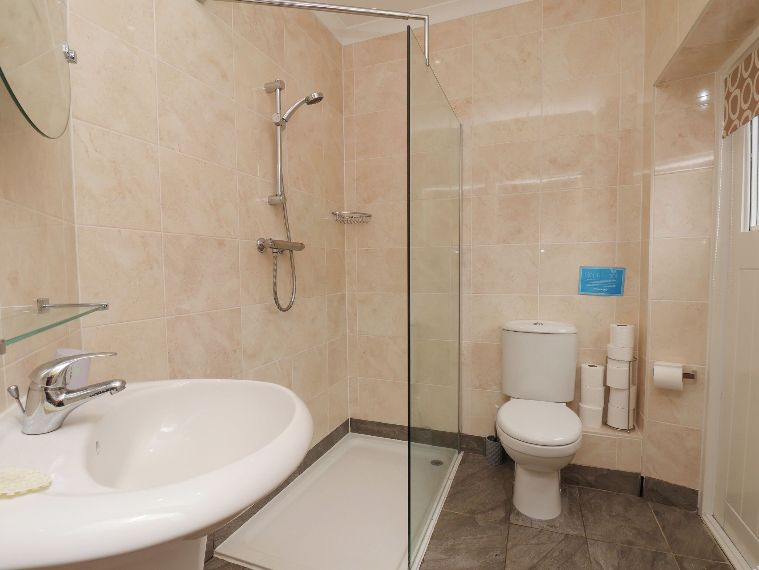 Un bany amb dutxa de vidre, un lavabo blanc i un vàter.