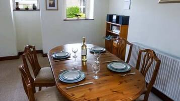 Uma sala de jantar com uma mesa de madeira posta para quatro pessoas, rodeada por cadeiras de madeira.