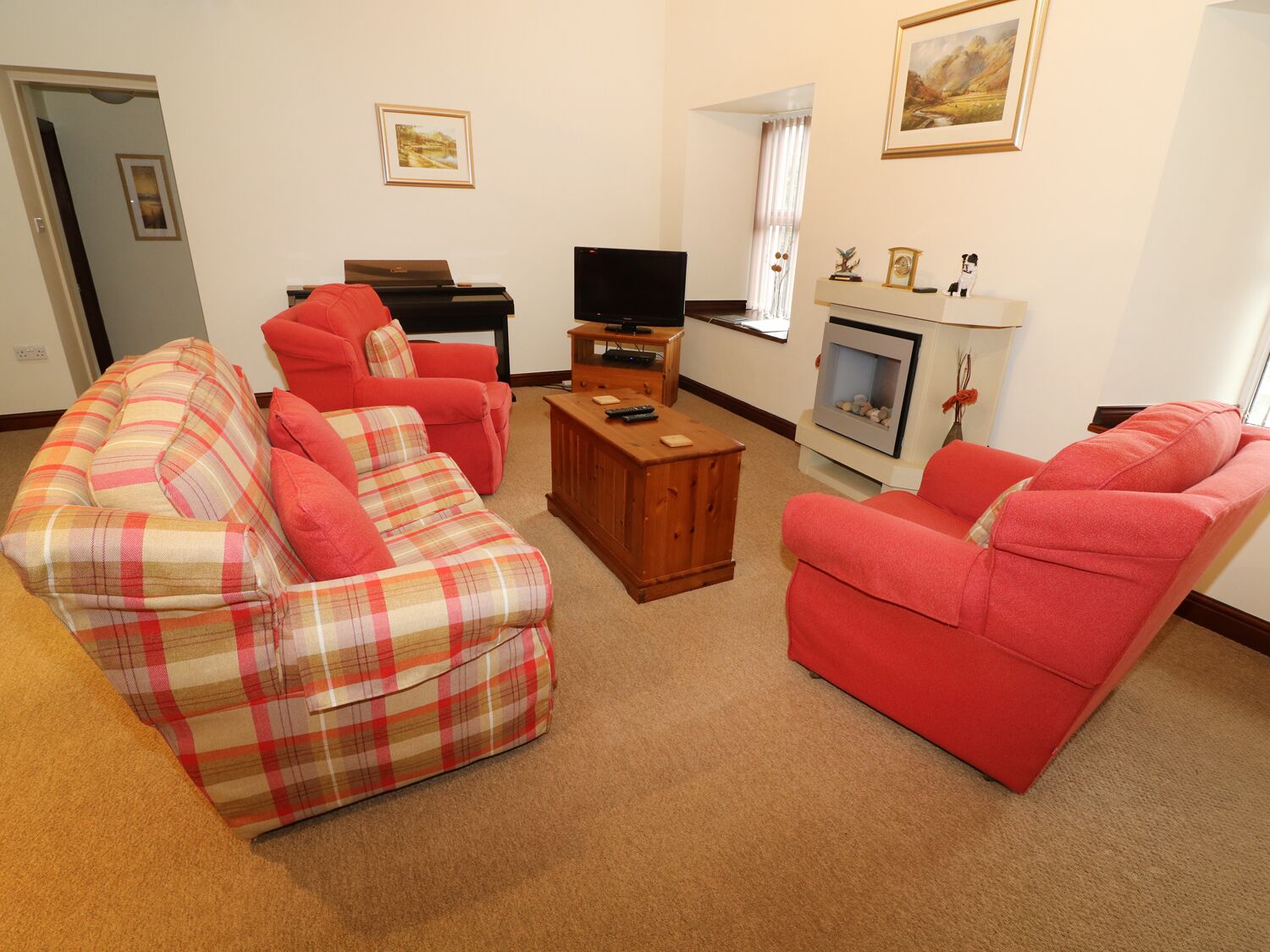 Een woonkamer met een geruite bank, een rode fauteuil, een houten salontafel, een flatscreen televisie en een open haard.