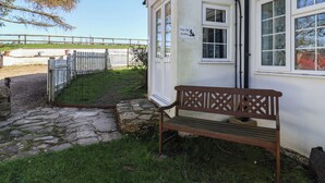 Ein weißes Gebäude mit einem Schild, auf dem 'The Old Smithy' steht, einer Holzbank, einem gepflasterten Weg und einem eingezäunten Bereich.