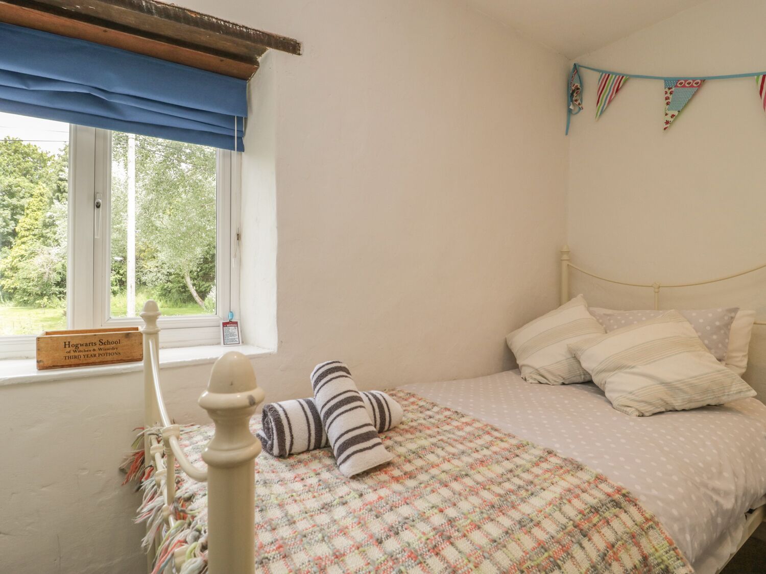 Una camera da letto con un letto, cuscini, una coperta, un cartello alla finestra e vista sul verde all'esterno.