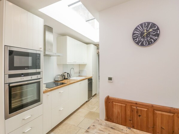 A modern kitchen with white cabinets, a microwave, an oven, a sink, and a wooden bench.