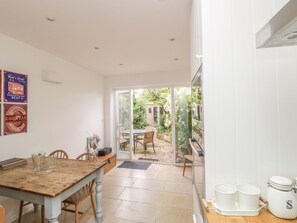 A kitchen with a wooden table, chairs, and a view of a garden through glass doors.