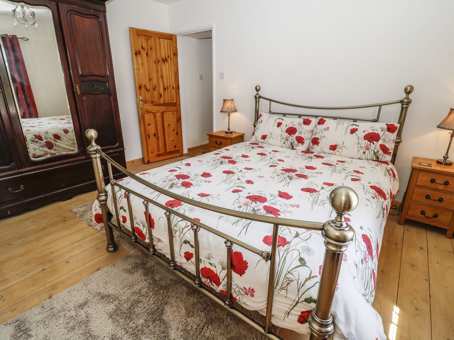 A bedroom with a bed, wooden wardrobe, and a mirror.