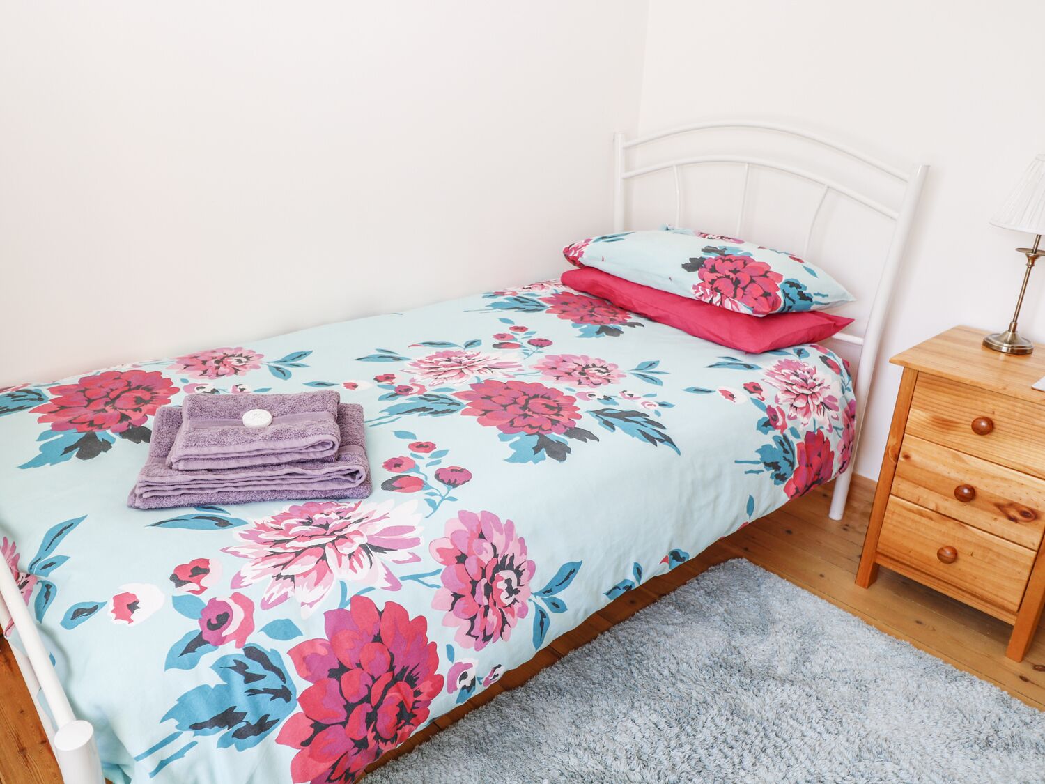 Una cama con una colcha estampada, una mesita de noche con una lámpara y un mueble con cajones.