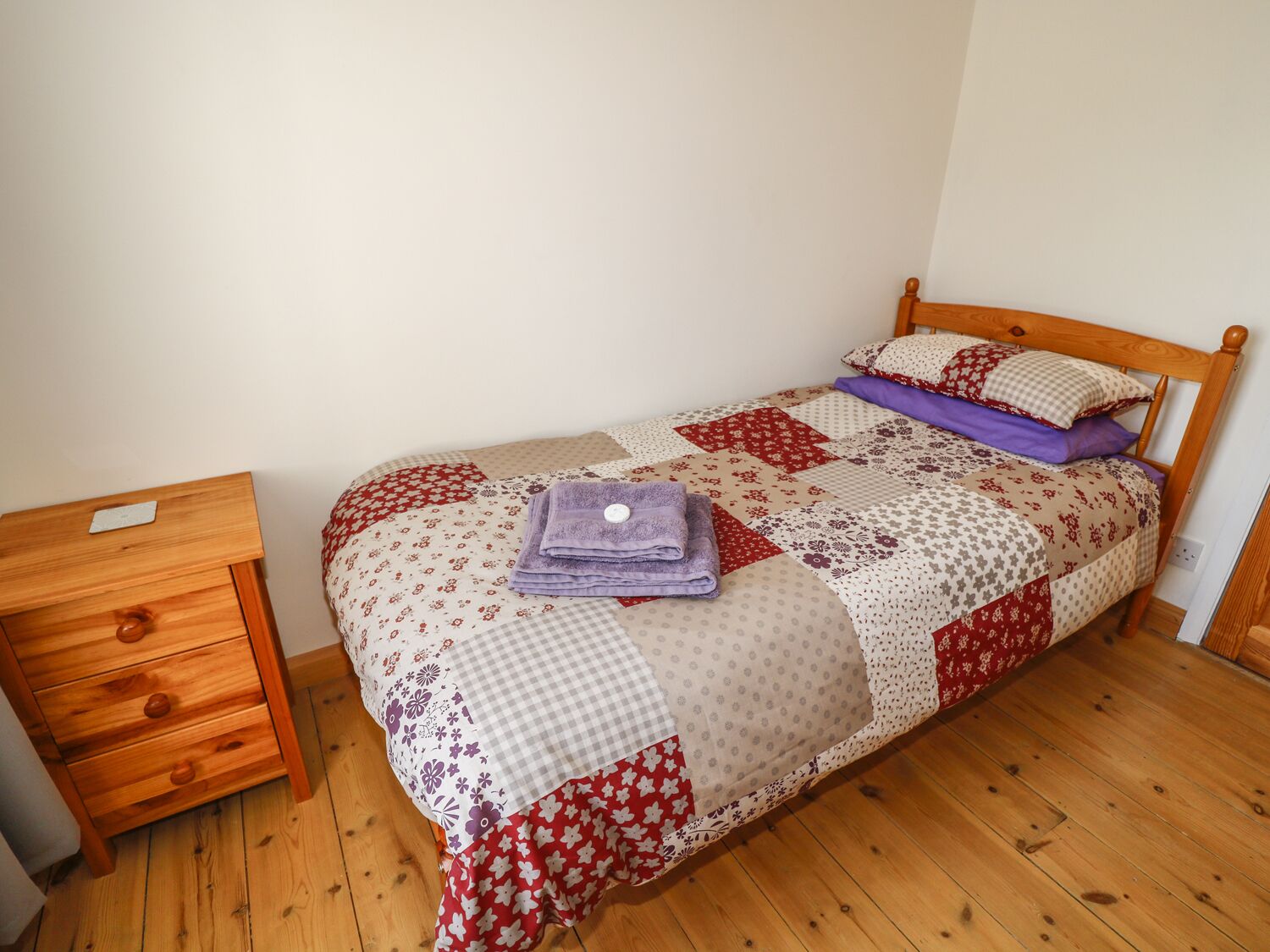 A single bed with a wooden headboard, a wooden nightstand with drawers, and a wooden floor.