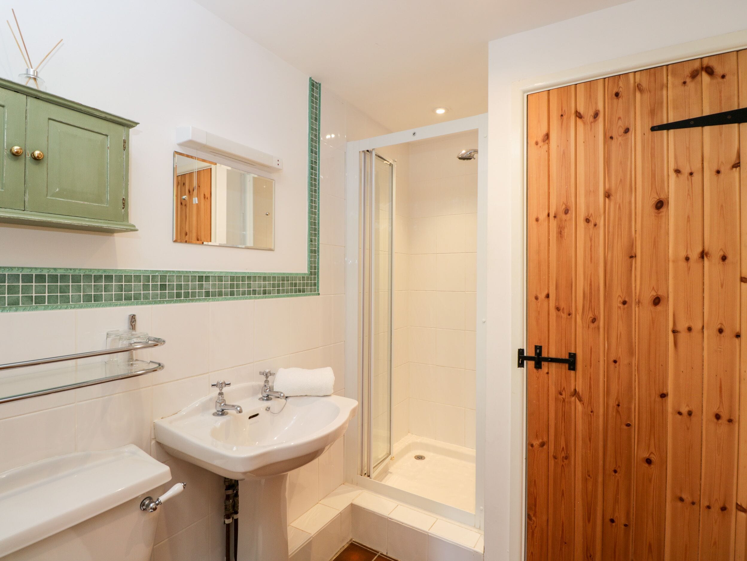 Un baño con lavamanos, espejo, armario y puerta de madera.