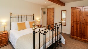 Un dormitorio con techo de madera, estructura de cama metálica, armario de madera y mesita de noche con lámpara.