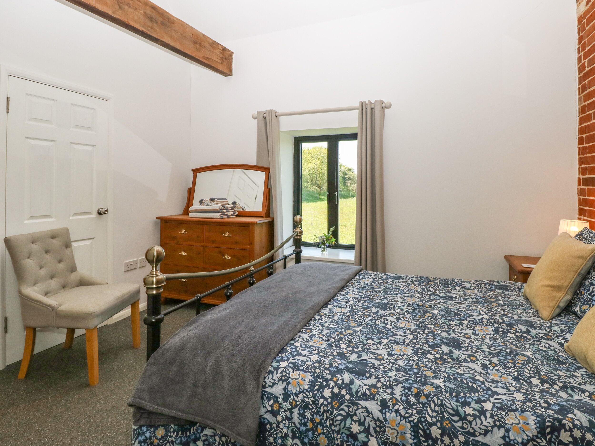 Un dormitorio con cama, una silla, un aparador y una ventana con vista a follaje.