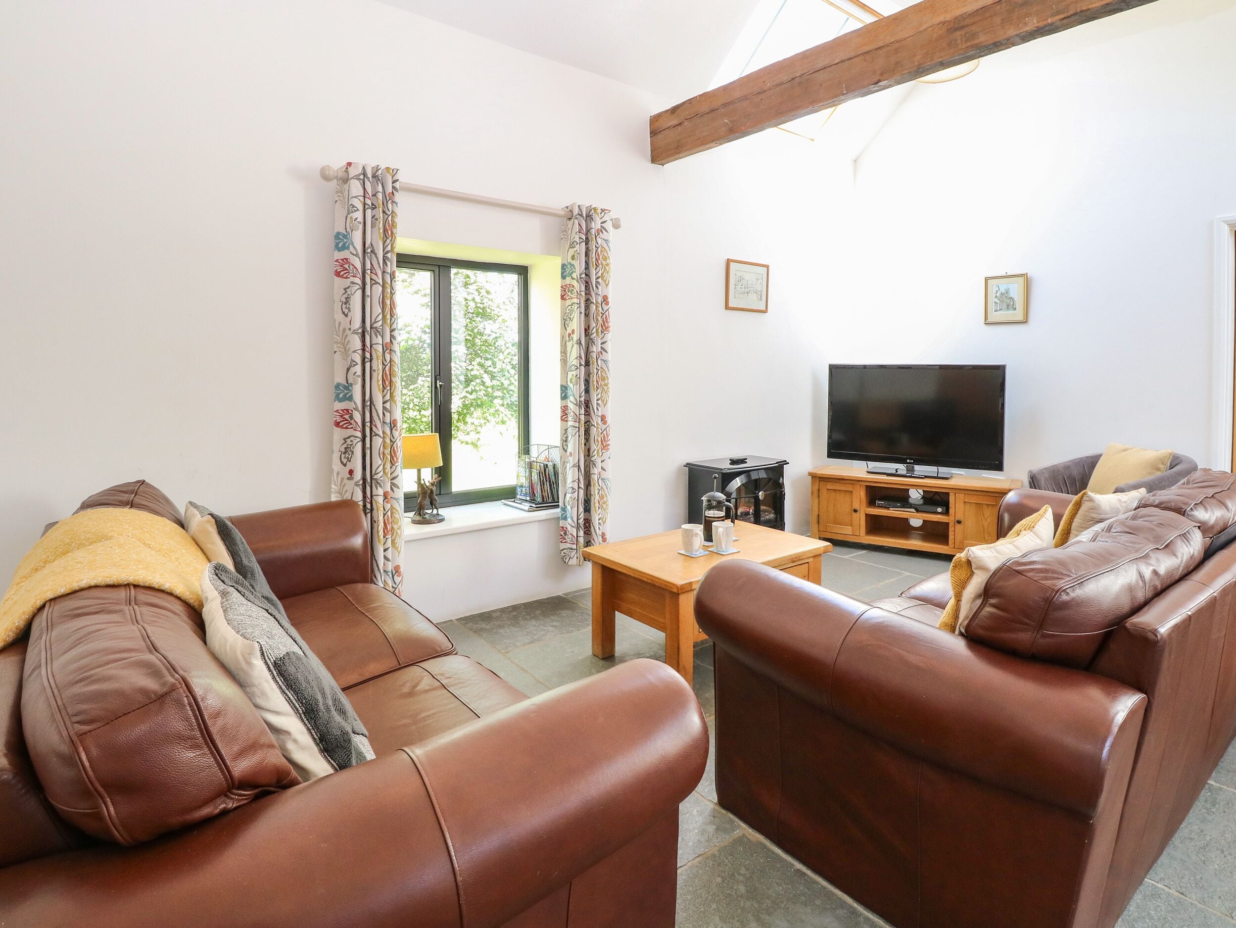 A living room with leather sofas, a wooden coffee table, a television, and a window with curtains.