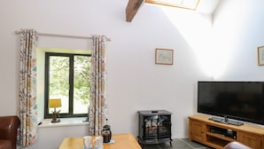 Una sala de estar con televisor, muebles de madera, una mesa con tazas, una ventana con cortinas y una chimenea.