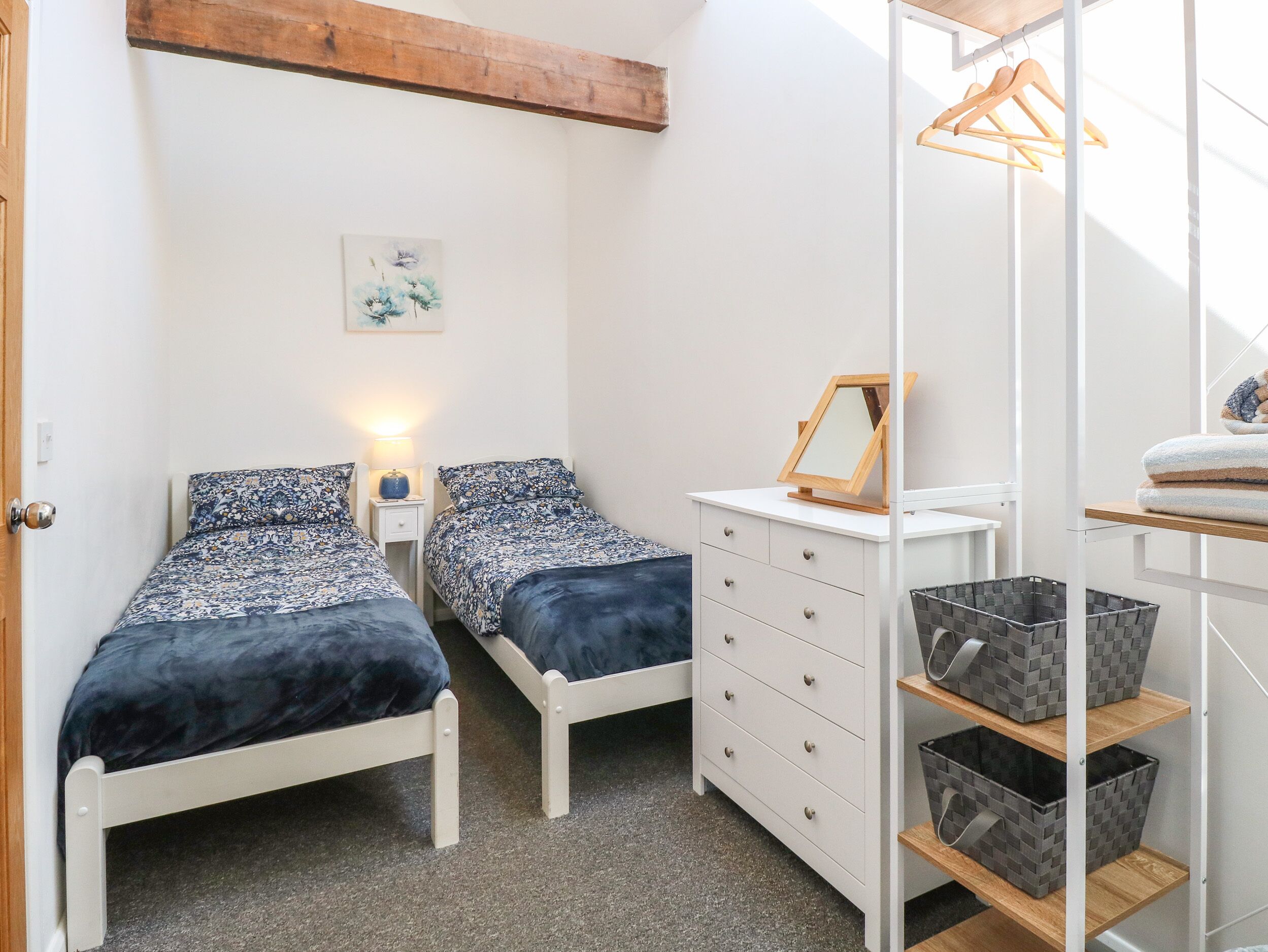 Un dormitorio con dos camas individuales, un tocador, un espejo y un perchero con ropa.