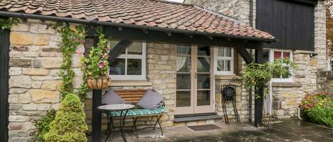 A stone building with a tiled roof, a bench, and a table outside.