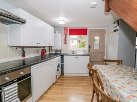 Cocina compacta con armarios blancos, horno empotrado, lavadora y zona de comedor con mesa y sillas.