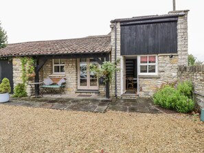 Une petite maison en pierre avec un toit en tuiles, un petit patio avec une table et des chaises, et une allée gravillonnée.