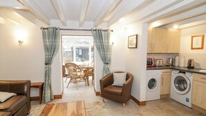 Una sala de estar acogedora con sofá, sillón y mesa de centro, un comedor con sillas y una cocina con lavadora y armarios.