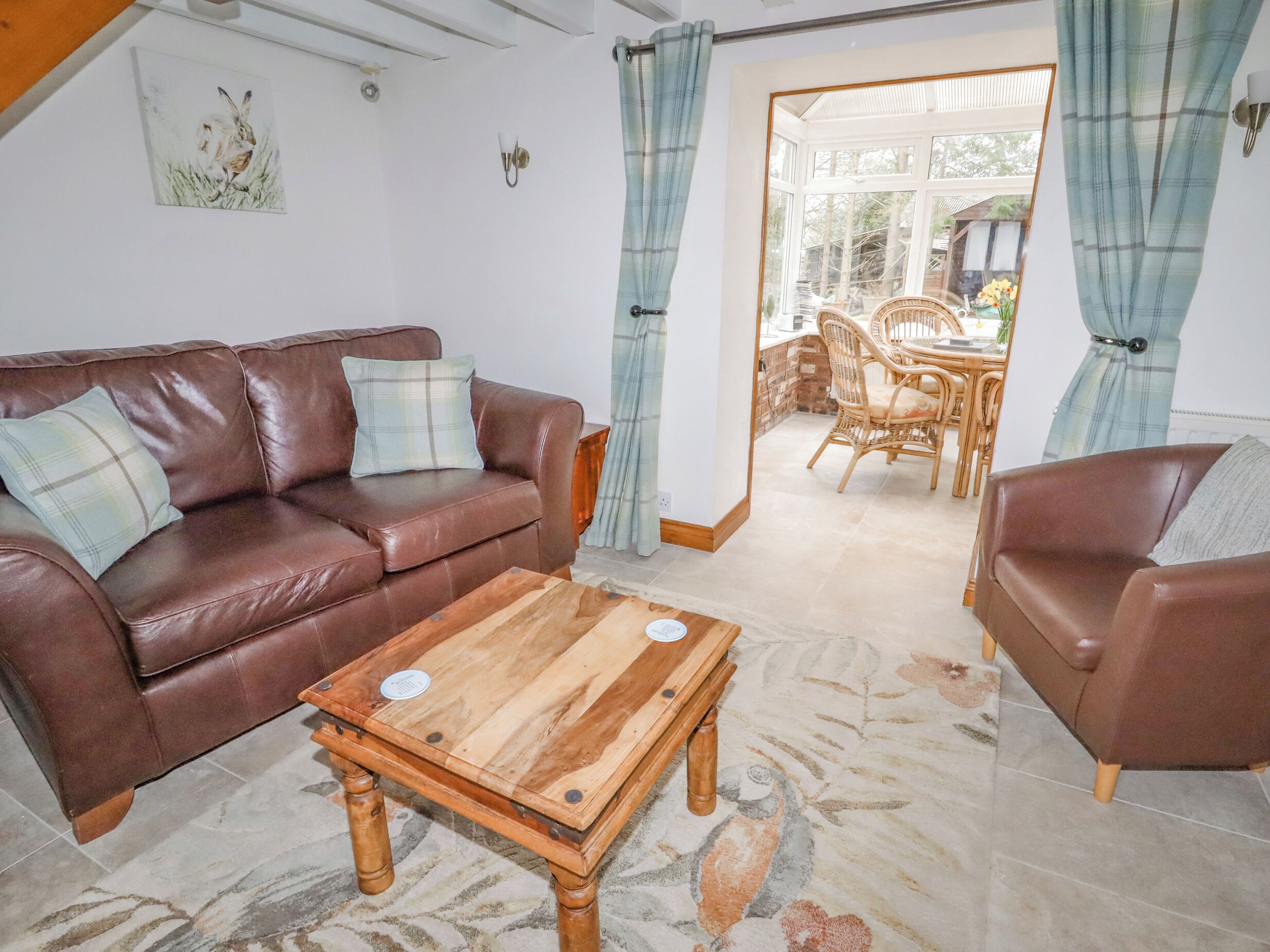 A living room with a brown leather sofa, a wooden coffee table, and a dining area with wicker furniture.