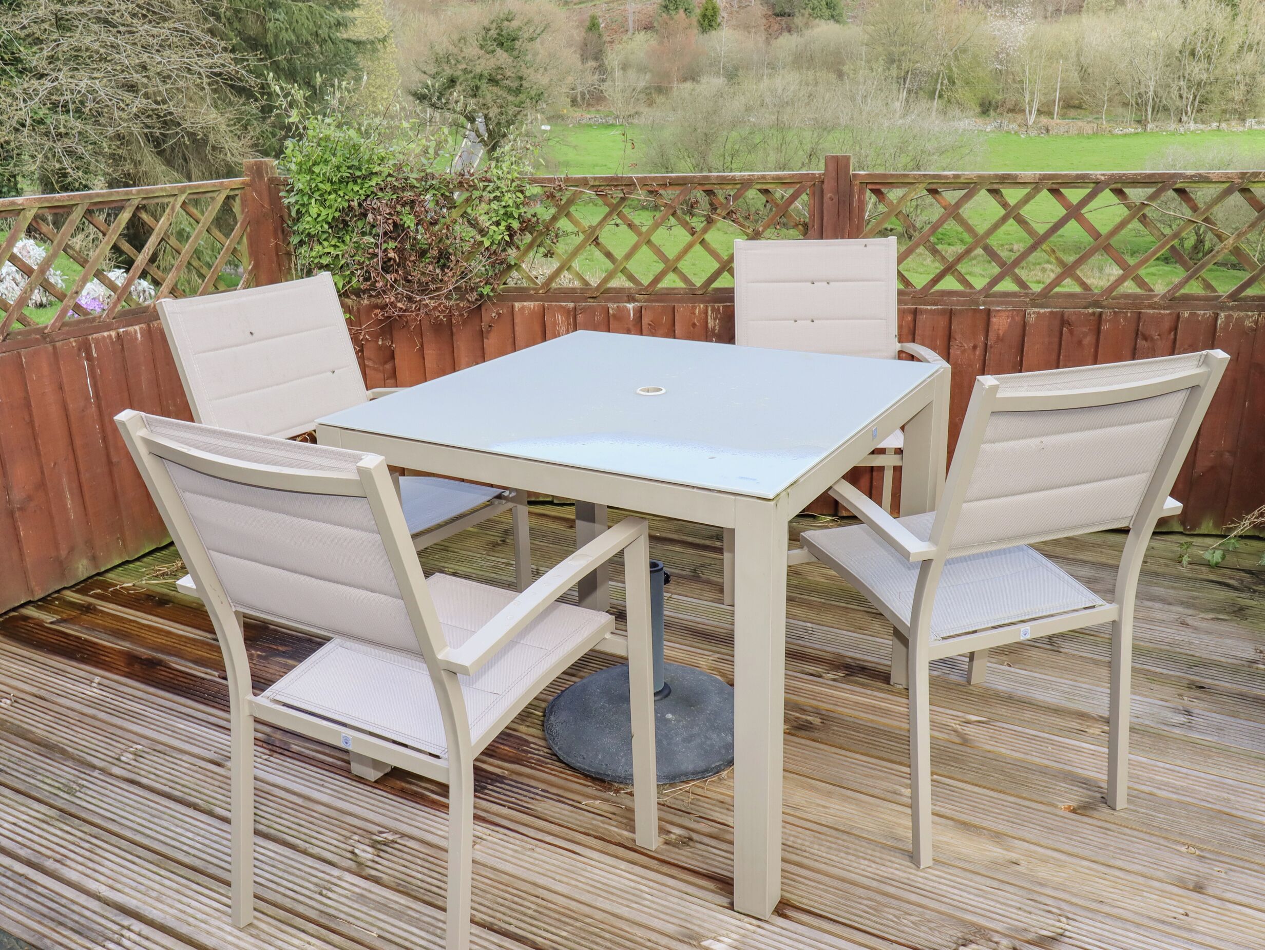 Eine Terrasse mit einem weißen Tisch und vier Stühlen, umgeben von einem Holzzaun und Grünpflanzen.