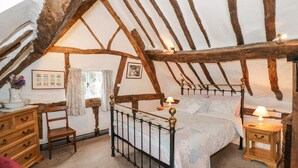 Une chambre avec un plafond en pente, des poutres apparentes, un lit à baldaquin, une commode en bois, une chaise et une table de chevet avec une lampe.