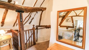 Une chambre avec des poutres apparentes, un cadre de lit en bois, une table de chevet avec une lampe et un miroir au mur.