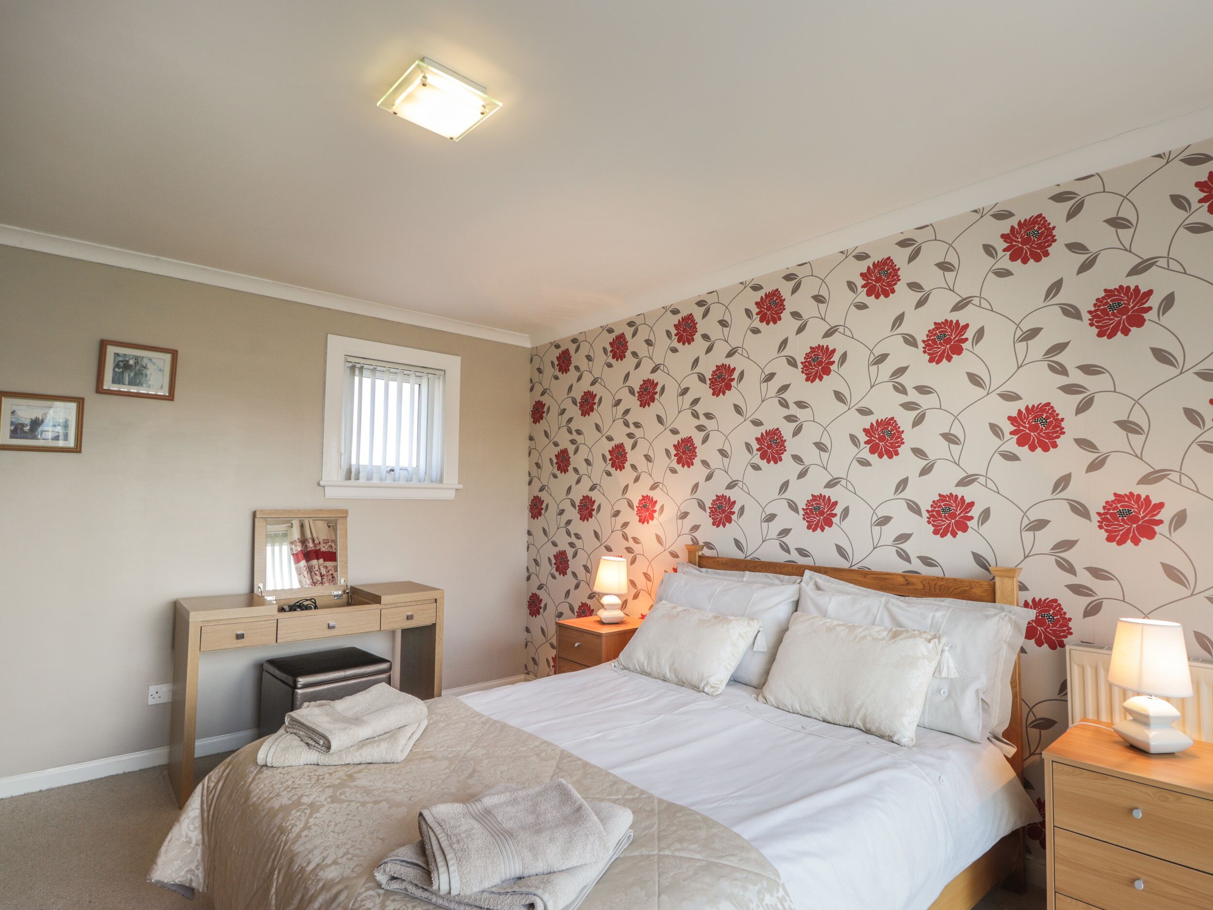 A bedroom with a bed, bedside tables, a desk, and a window.