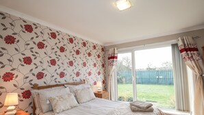 Une chambre à coucher comprenant un lit, des tables de chevet, une lampe et une vue sur un jardin à travers une porte-fenêtre coulissante.