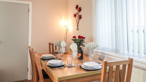 Une table à manger dressée avec des assiettes, des verres et des couverts, un vase rempli de fleurs et une bouteille de champagne.